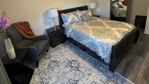 A bedroom with a bed, nightstands, a chair, a rug, a ceiling fan, and a mirror. - Elegant and cozy  5 1/2 appartement with pool (Longueuil)