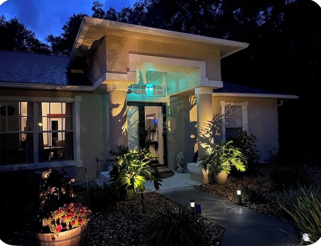 A modern house with a well-lit entrance, a stone statue, and potted plants.