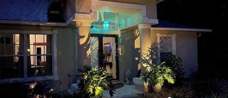 A modern house with a well-lit entrance, a stone statue, and potted plants.