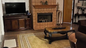 Een woonkamer met een open haard, een televisie en een plafondventilator.