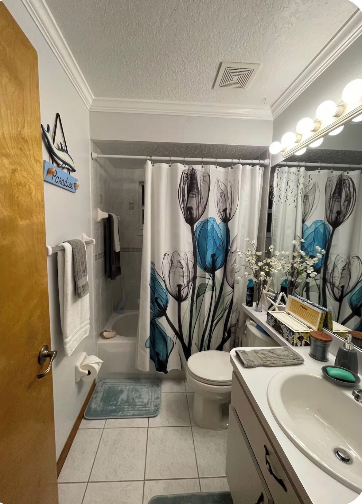 A bathroom with a shower curtain, toilet, sink, and a mirror with lights.