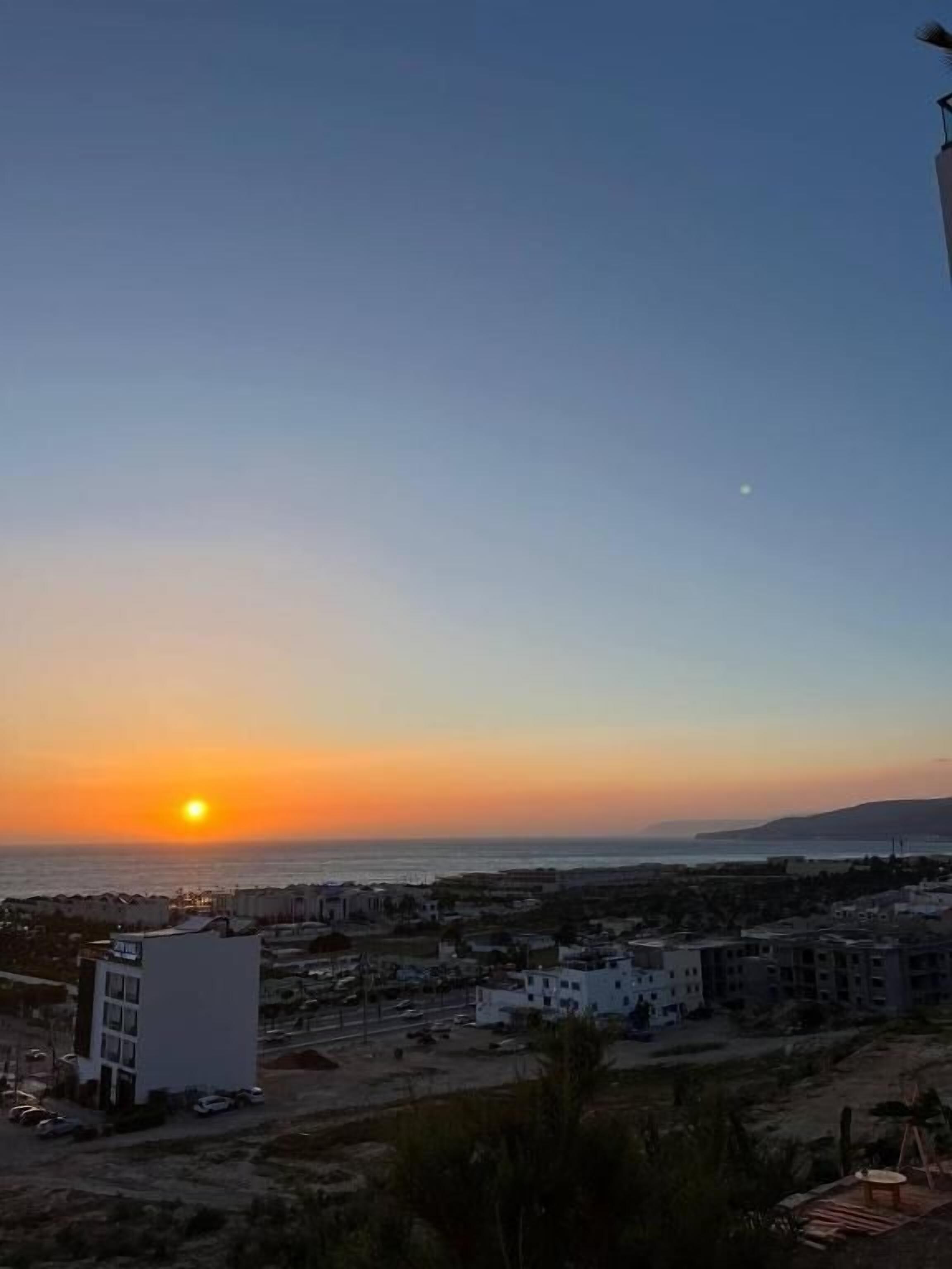 A coastal cityscape at sunset with buildings and a clear sky.