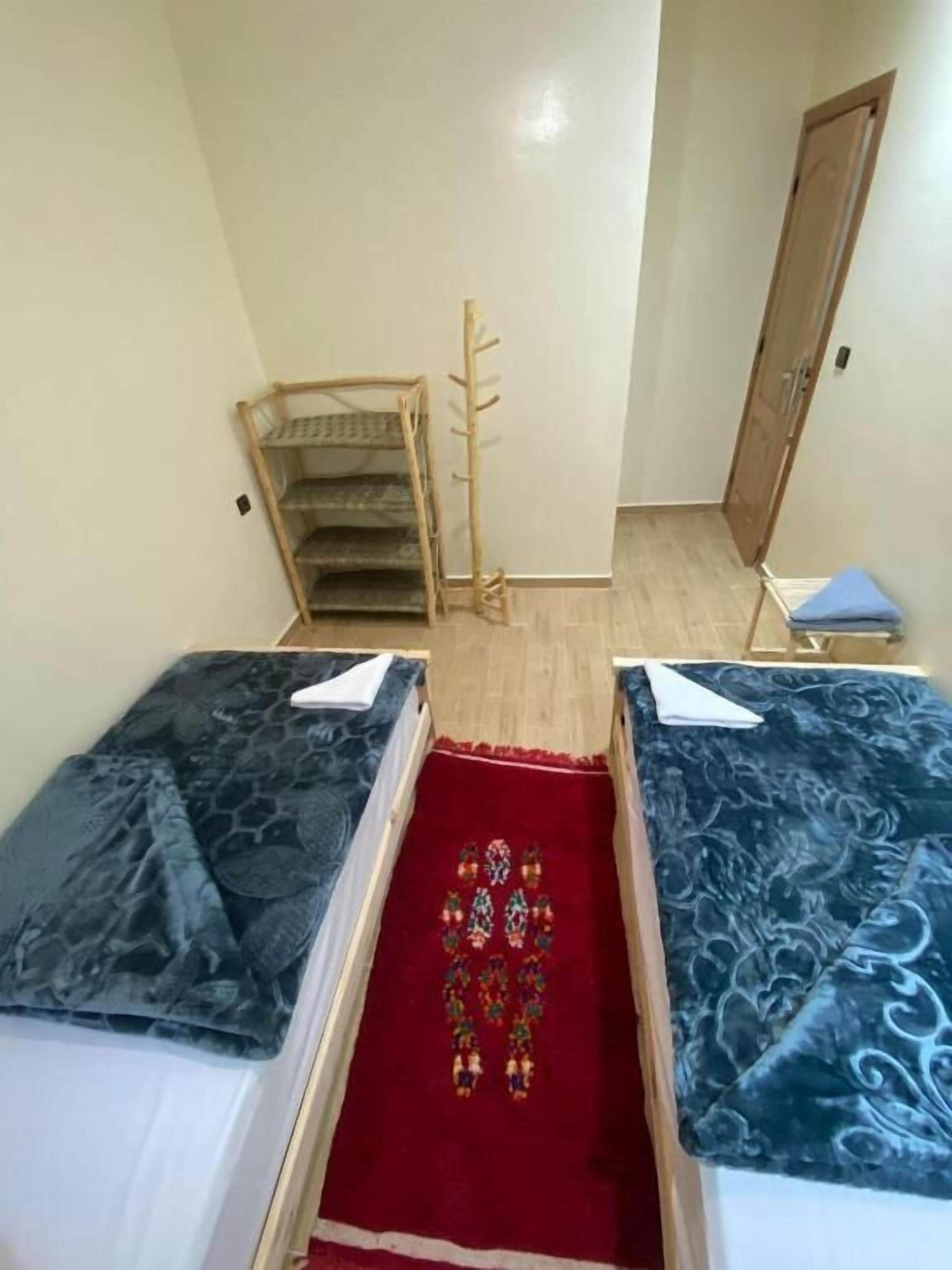 Una habitación con dos camas, una escalera de madera, una puerta y un tapete rojo con diseño.
