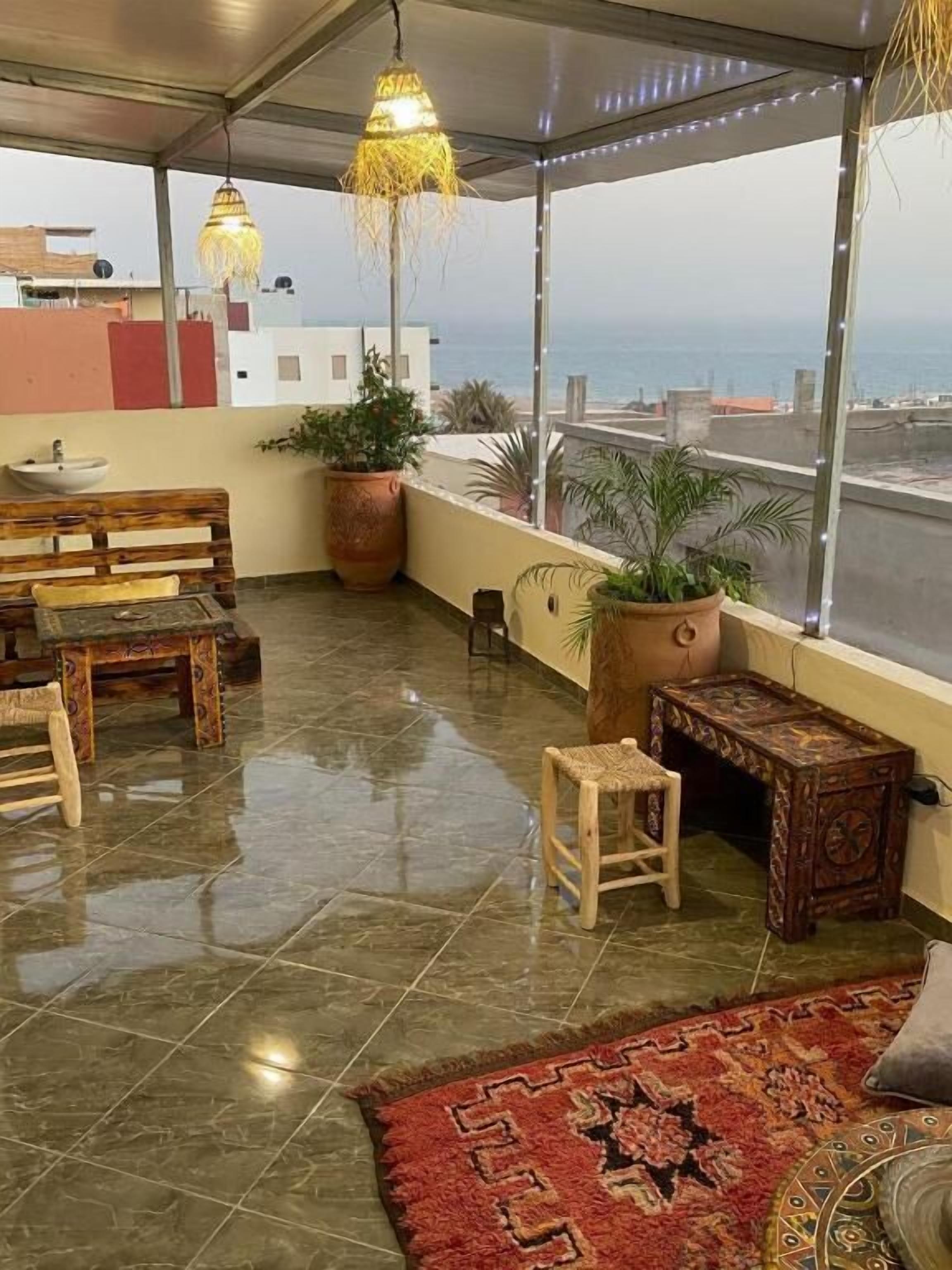 Une terrasse sur le toit avec un banc en bois, une petite table, des plantes en pot et une vue sur la mer.