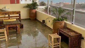Une terrasse sur le toit avec un banc en bois, une petite table, des plantes en pot et une vue sur la mer.