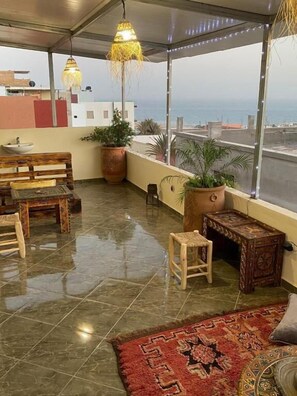 A rooftop terrace with a wooden bench, a small table, potted plants, and a view of the sea. - Breeze Surf Lodge (Tamraght)