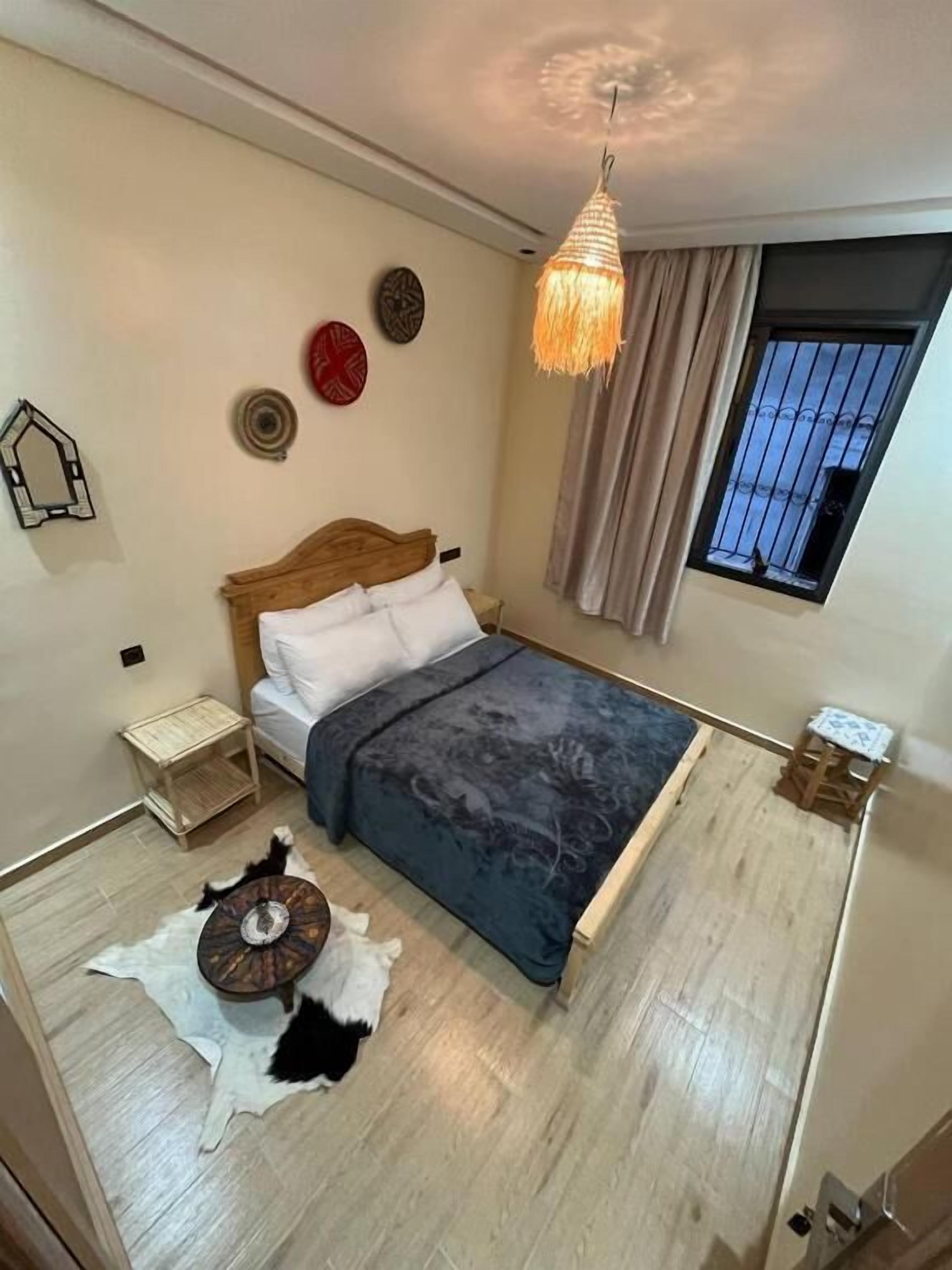 A bedroom with a bed, a small bedside table, a round rug, and a window with curtains.