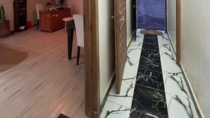 Un couloir avec un sol carrelé, un cadre de porte en bois et un luminaire au plafond.
