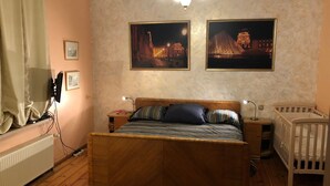 A bedroom with a wooden bed, bedside tables, a crib, and two framed pictures on the wall. - Classical large apartment on art deco Alberta street, FREE locked PARKING (Rīga)