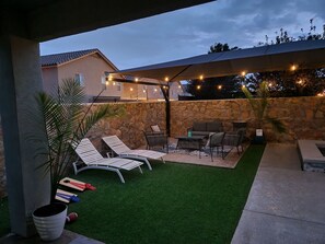Eine Terrasse mit Gartenmöbeln, einer Steinmauer und Lichterketten.