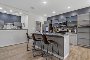 Cozinha moderna com ilha central, banquetas, eletrodomésticos de aço inoxidável e painel de parede cinza.