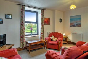 A living room with a television, a red armchair, a wooden coffee table, and a window with floral curtains. - Retreat Near National Parks (Torrington)