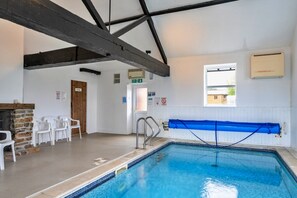 Ein Hallenbad mit Steinwand, weißen Stühlen, einer blauen Rettungsschwimmerleiter und einem Fenster mit Aussicht.