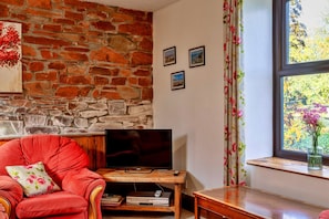 A living room with a stone wall, a red armchair, a television, and a window with a view of trees. - Retreat Near National Parks (Torrington)
