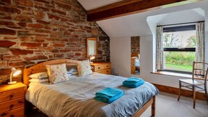 A bedroom with a brick wall, a wooden bed, a nightstand with a lamp, a dresser, a window with curtains, and a chair. - Retreat Near National Parks (Torrington)