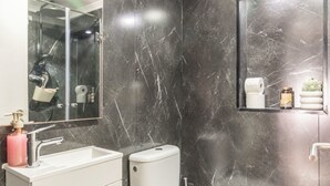Um banheiro moderno com parede de mármore, pia branca, vaso sanitário e espelho.
