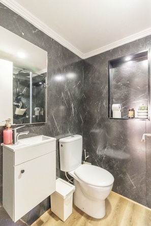 Ein modernes Badezimmer mit Marmorwand, Waschbecken in Weiß, Toilette und Spiegel.