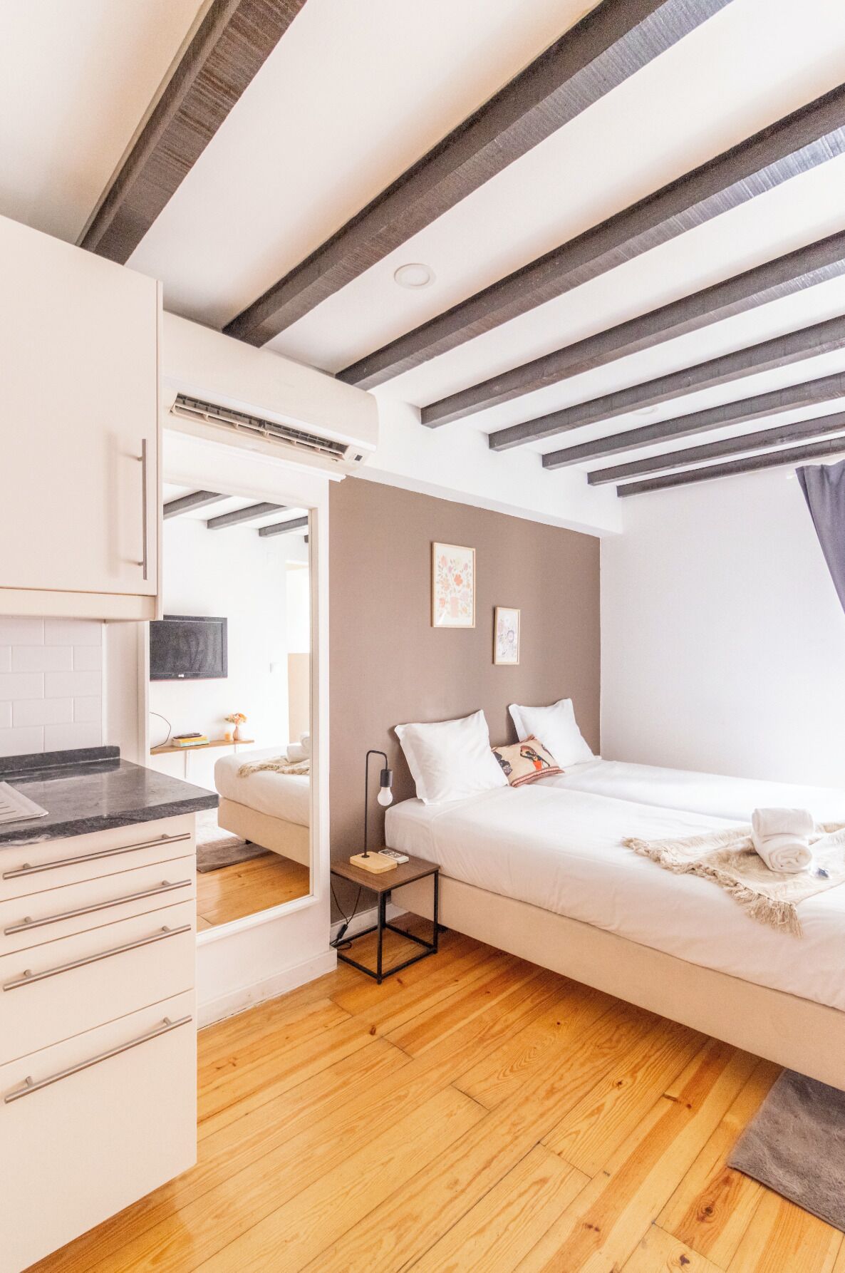 Une chambre moderne avec un lit en mezzanine, un plancher en bois, une armoire intégrée et un plafond avec des poutres apparentes.