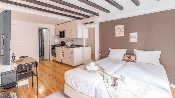 Quarto de hotel com cama, secretária com cadeira, cozinha compacta e banheiro.