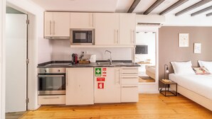 Cozinha compacta com micro-ondas, forno e pia, que dá acesso a um quarto com cama e mesa de cabeceira.