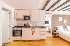Eine kleine Küche mit Mikrowelle, Backofen und Spüle, die in einen Schlafbereich mit Bett und Nachttisch übergeht.