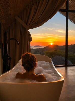 Eine Badewanne voller Blasen, ein Fenster und Blick auf einen Sonnenuntergang.