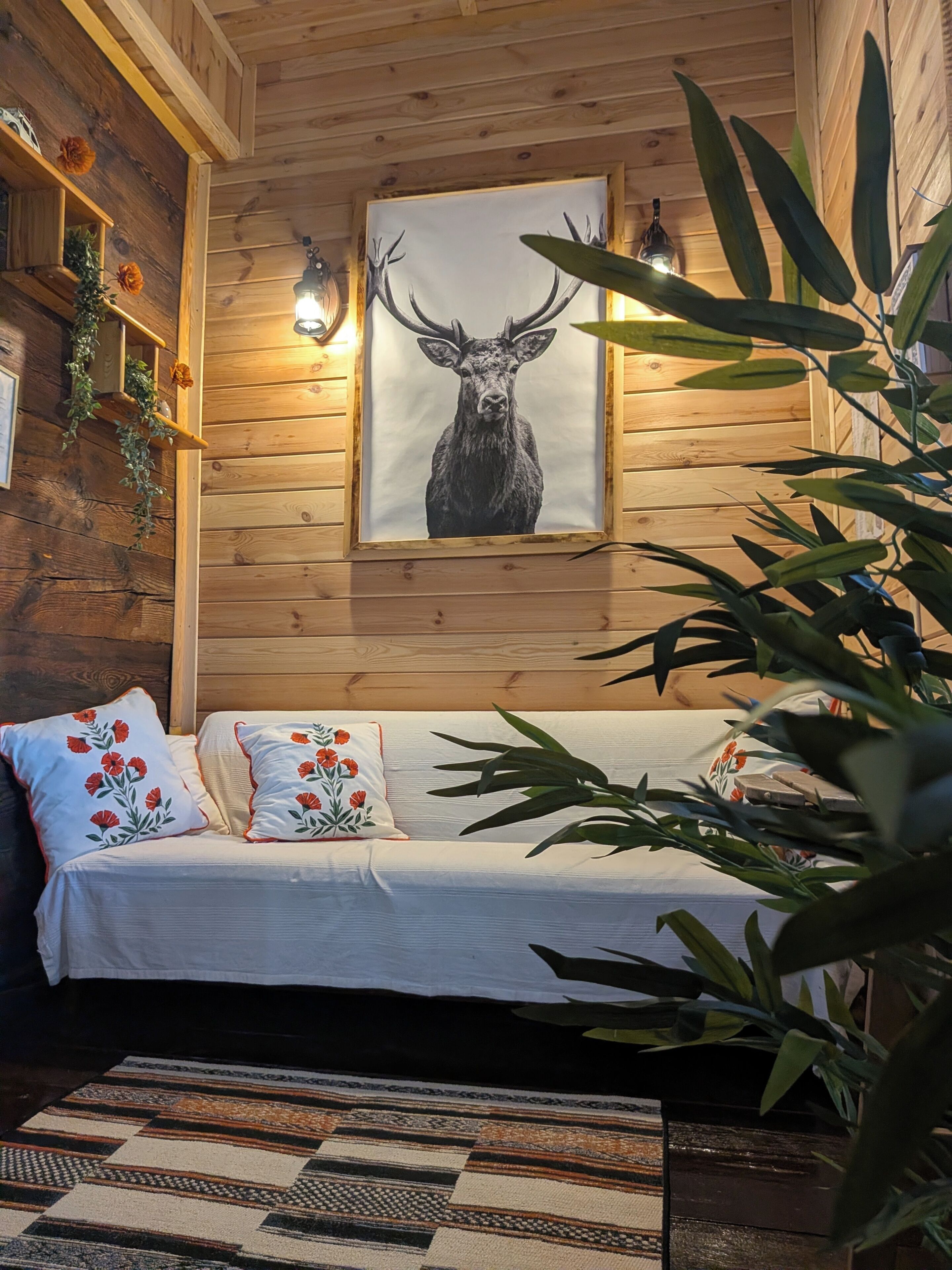 A wooden interior with a sofa, decorative pillows, a framed deer artwork, and a plant.