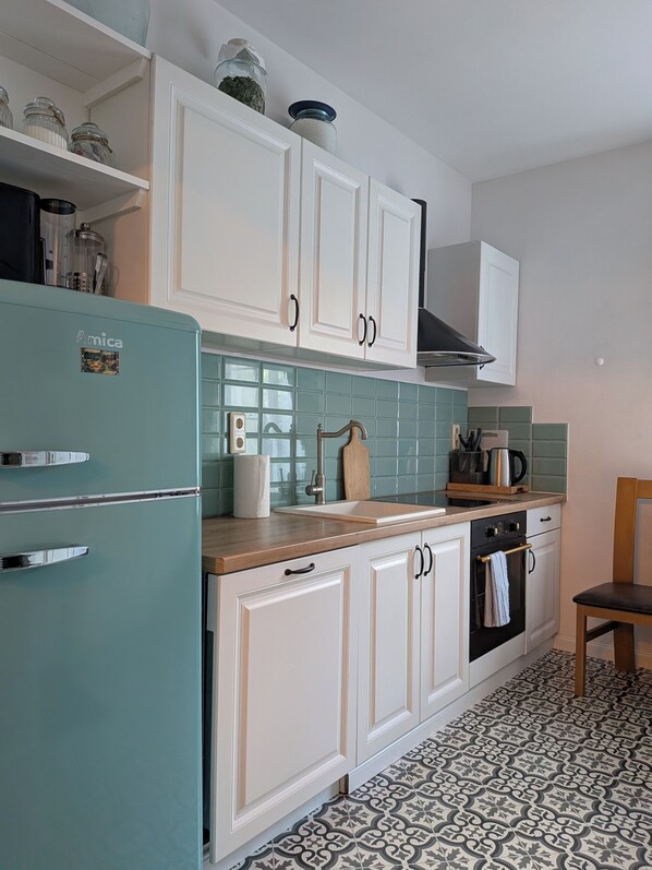 A kitchen with white cabinets, a teal refrigerator, a patterned backsplash, and a wooden chair. - Kierunek Puszcza 2 Apartments - Hot Tub, Sauna, Salt Cave - max. 14 people (Narewka)