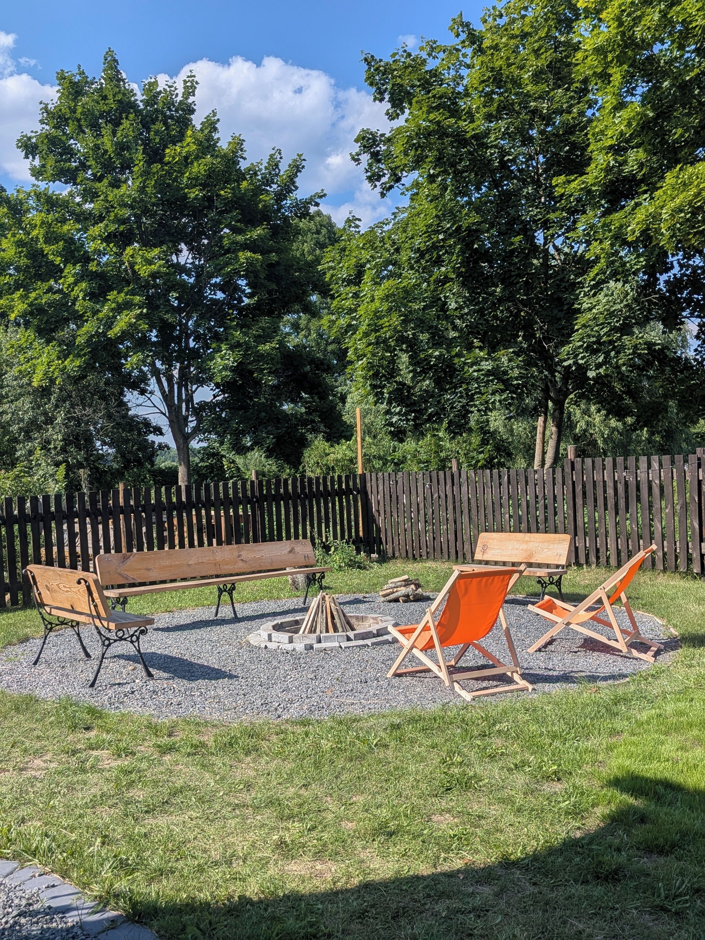 A backyard with a wooden bench, orange chairs, and a fire pit.