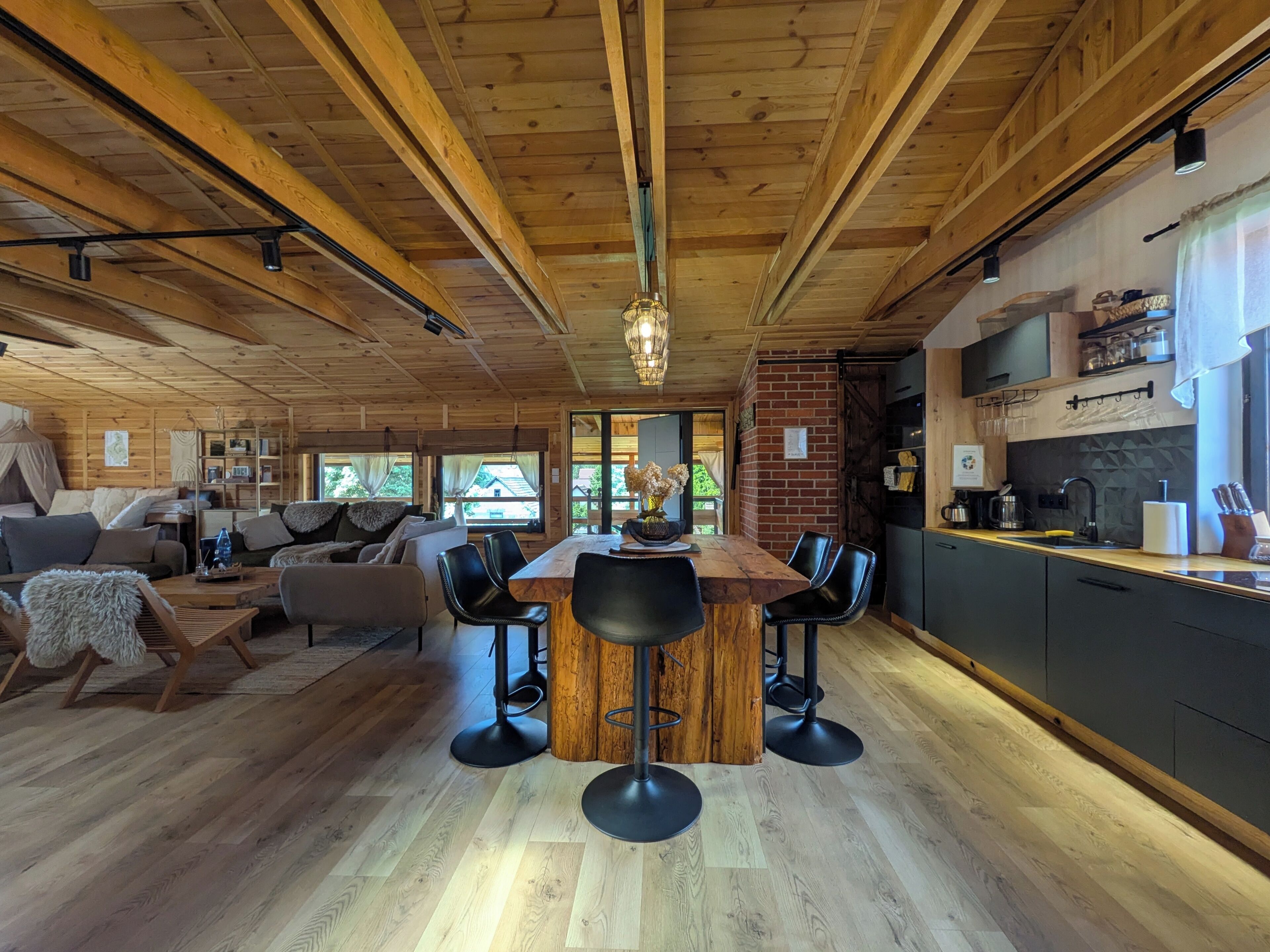 A spacious living area with a wooden ceiling, a dining table with chairs, a sofa, and a kitchen area with modern appliances.