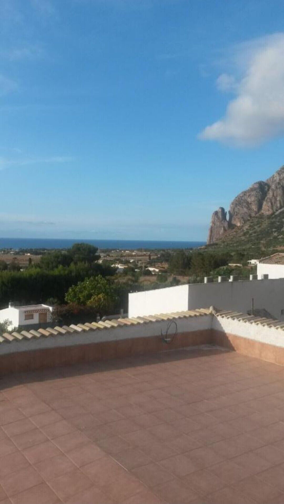 A rooftop terrace with a view of the sea and a mountain.