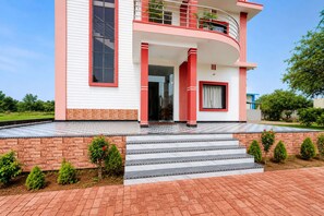 Un edificio de dos pisos con fachada roja y blanca, un balcón en el nivel superior y una escalera que conduce a la entrada.