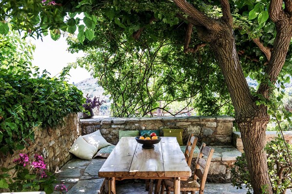 A rustic wooden table with a bowl of fruit, surrounded by stone walls and lush greenery. - Kamares Boutique Suite in a Restaured Venetian Domain (Apokoronas)