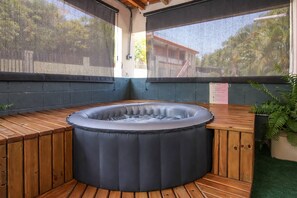 A hot tub with a wooden bench surrounding it, set against a backdrop of a house and greenery. - Casa Isabel en Calvache Rincon PR for 6 people. (Rincon)
