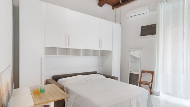 Um quarto com cama, uma mesa de madeira, uma cadeira e um guarda-roupa.