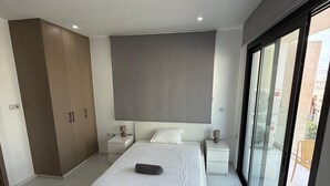 Ein modernes Schlafzimmer mit einem großen Bett, einem Kleiderschrank, einem Nachttisch und einer Glastür zum Balkon.