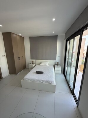 A modern bedroom with a large bed, a wardrobe, a bedside table, and a sliding glass door to a balcony. - Modern business studio in central Larnaca - AC, WiFi, elevator (Larnaka)