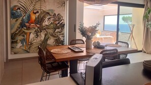 Zona de menjador amb un mural tropical gran, una taula amb cadires i vista a l'oceà a través d'una porta de vidre.