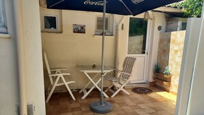 En terrasse med et bord, stole, en potteplante og en dør.