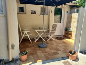 Eine Terrasse mit Tisch, Stühlen und einem Blumentopf, sowie einer Tür.