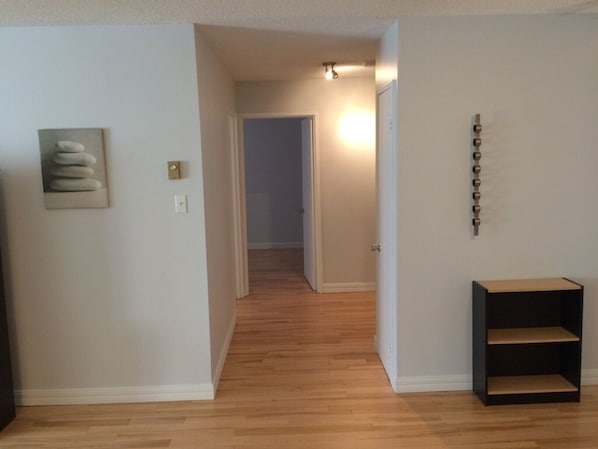 A hallway with wooden flooring, a door at the end, and a black shelf on the right.