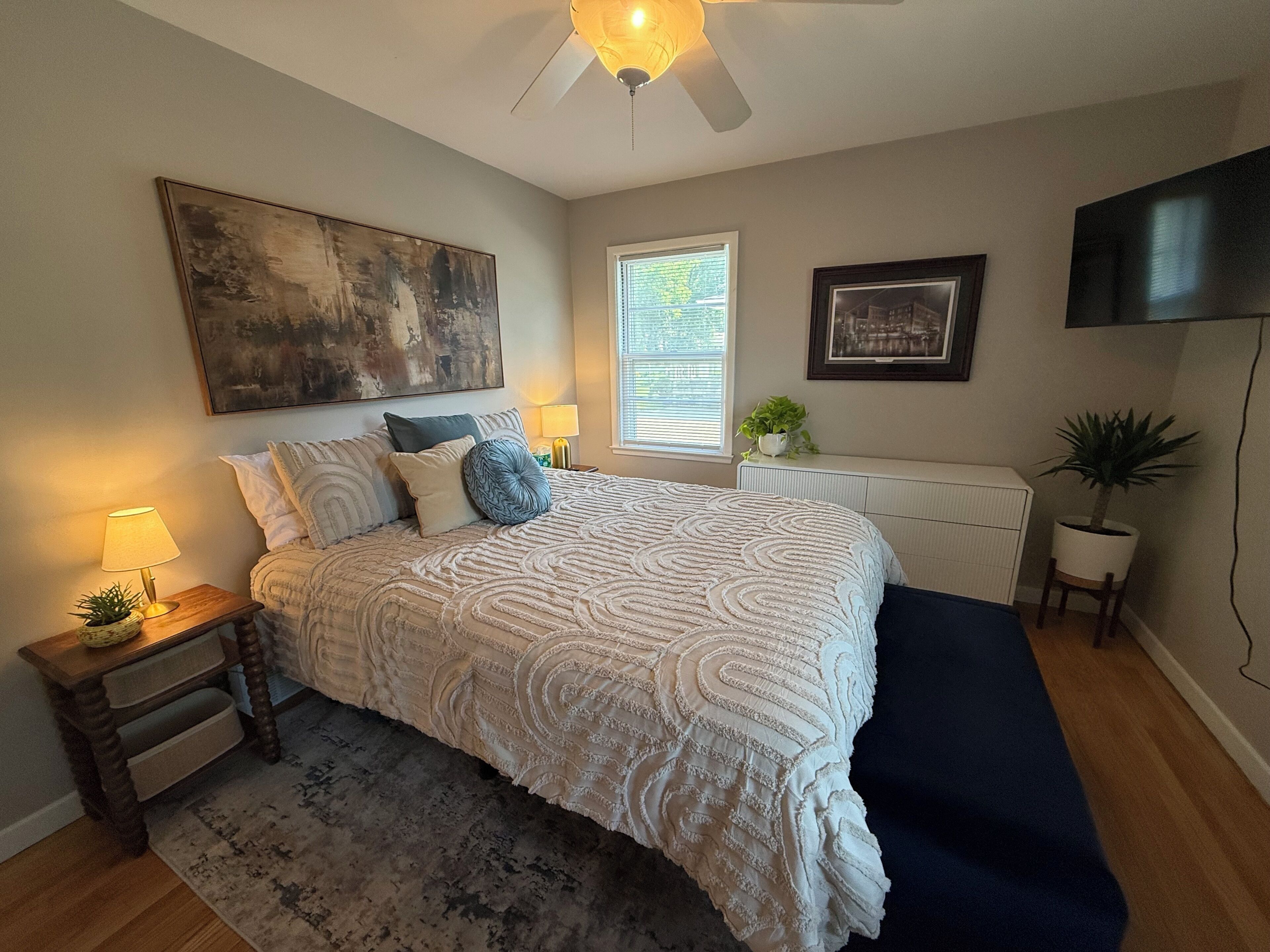 Une chambre à coucher comprenant un lit, des tables de chevet, un radiateur, un ventilateur de plafond, une télévision et une fenêtre.