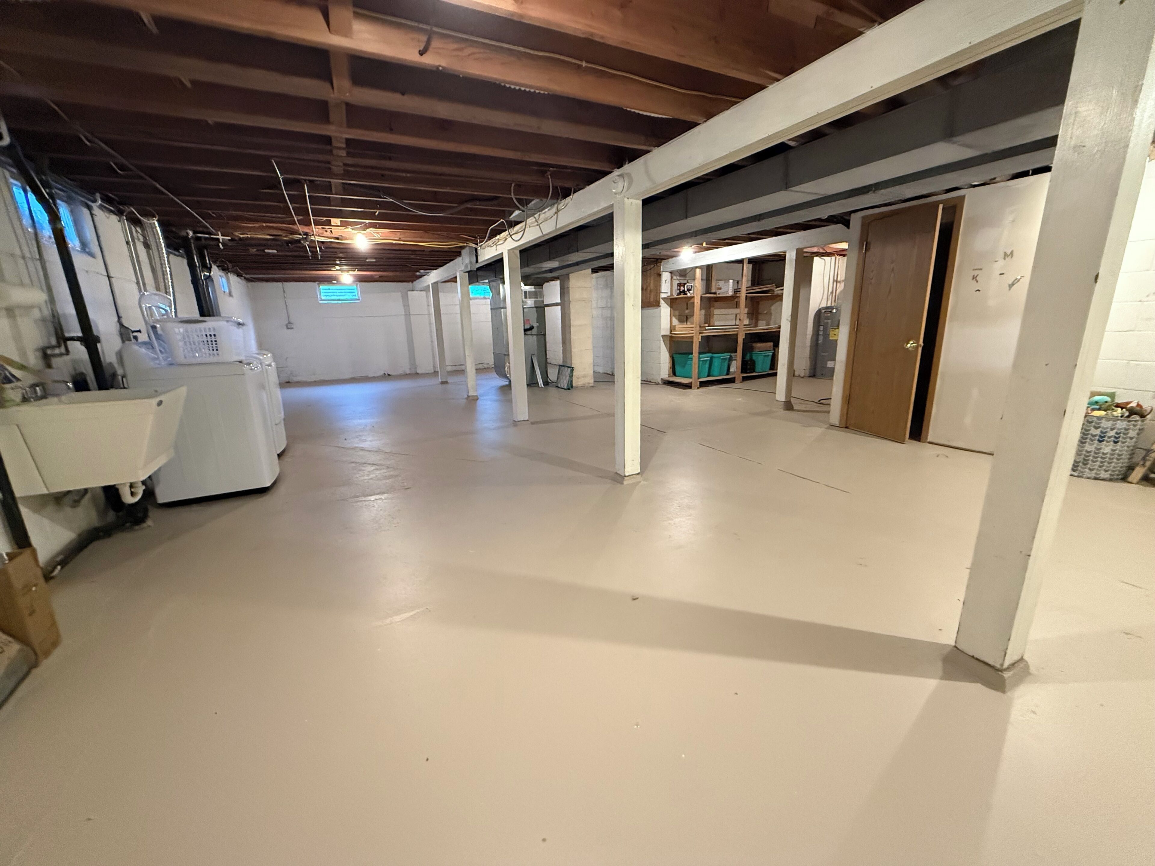 Een ruime, goed verlichte gang met een hoge plafond, witte muren en een schone vloer. Er zijn houten balken en kolommen, en een deur die naar een andere kamer leidt.