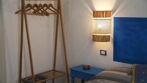 A bedroom with a wooden clothes rack, a bedside table with a small figurine, a wall-mounted lamp, and a large blue painting on the wall. - PROFUMO DI CALICANTO B&B (Tresnuraghes)