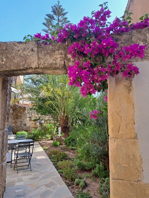 A stone archway with vibrant purple bougainvillea flowers, a stone pathway, and a seating area with chairs. - PROFUMO DI CALICANTO B&B (Tresnuraghes)