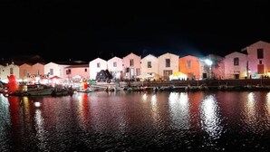 A waterfront property with multiple buildings, a dock with boats, and a calm water body reflecting the lights. - PROFUMO DI CALICANTO B&B (Tresnuraghes)