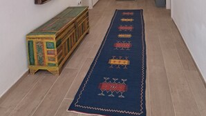 A hallway with a patterned rug, a wooden cabinet, a mirror, and a door. - PROFUMO DI CALICANTO B&B (Tresnuraghes)