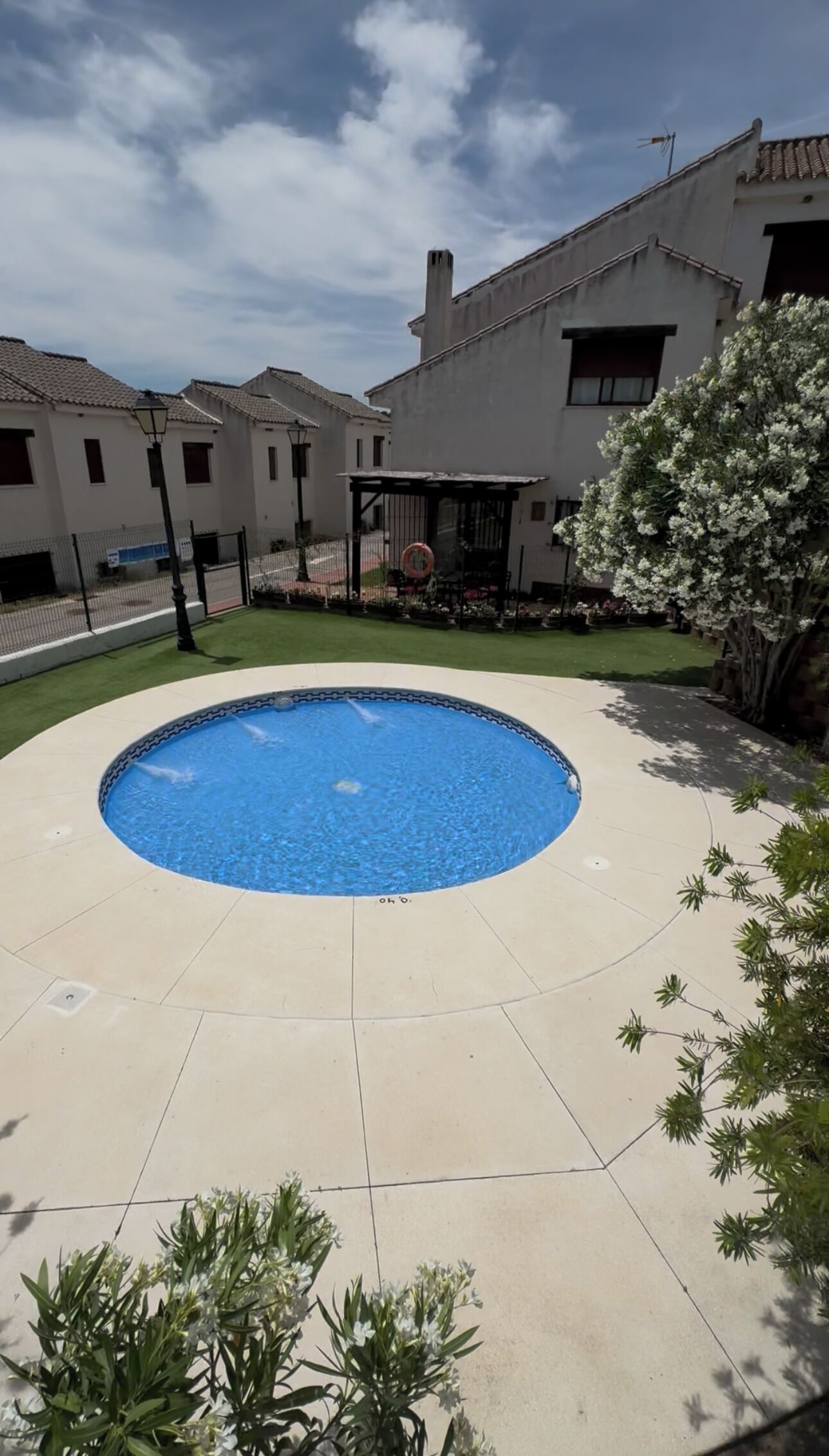 A swimming pool with a tiled deck, surrounded by a fence and a building with a tiled roof.