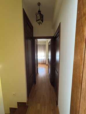 A hallway with wooden doors, a wooden floor, and a hanging light fixture.