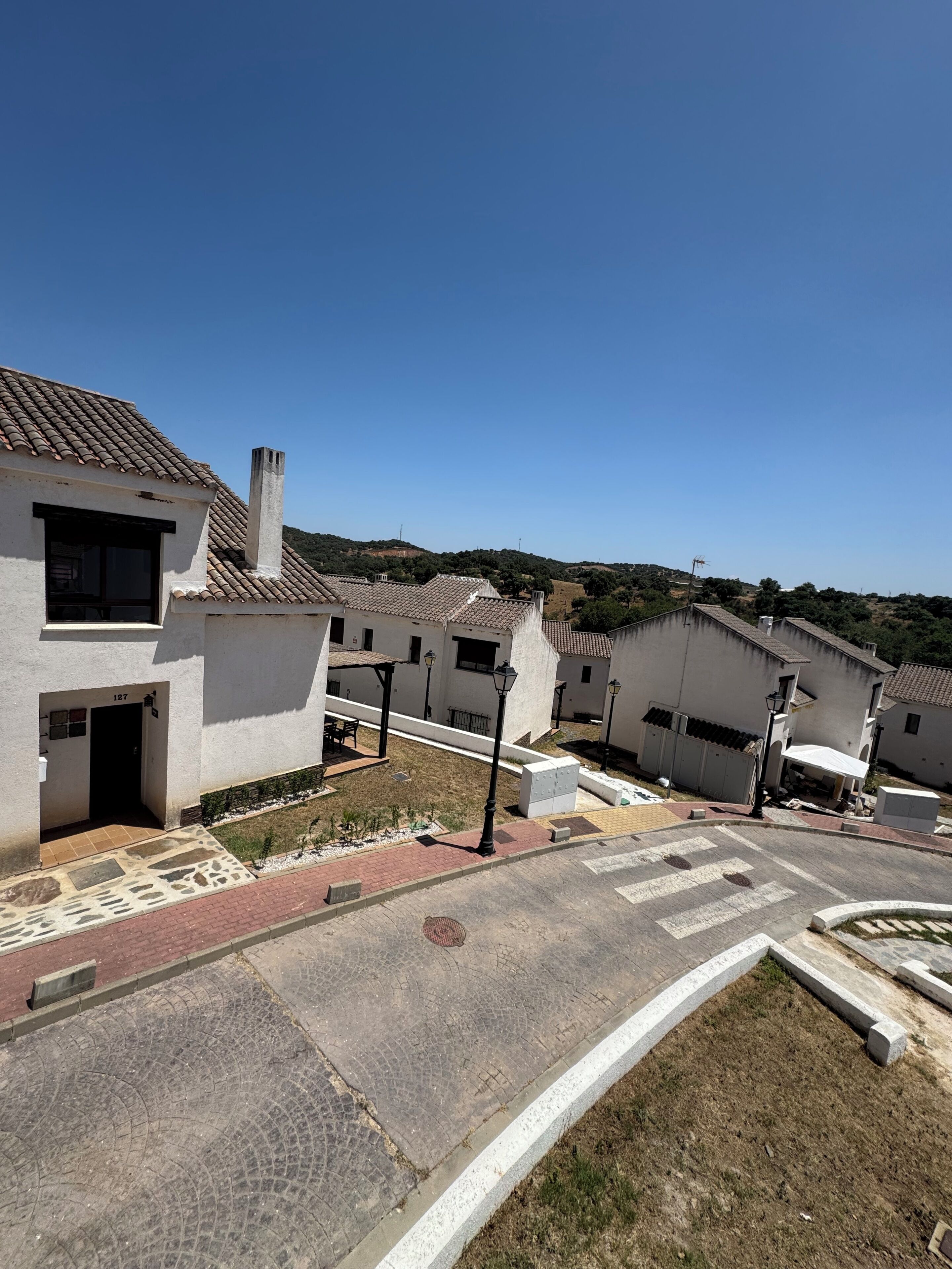 A residential area with white buildings, a paved street, and a clear sky.